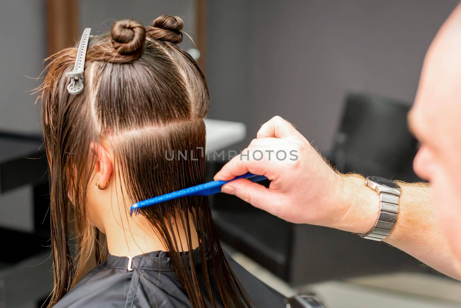 Rear View of male hairdresser combing wet hair of young caucasian woman divides into sections in a hair salon