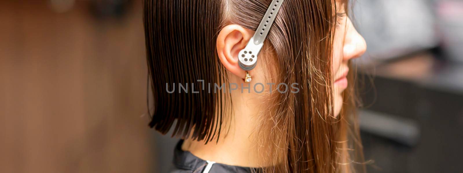 Close up side view of young brunette caucasian woman with split hair in sections in a hair salon