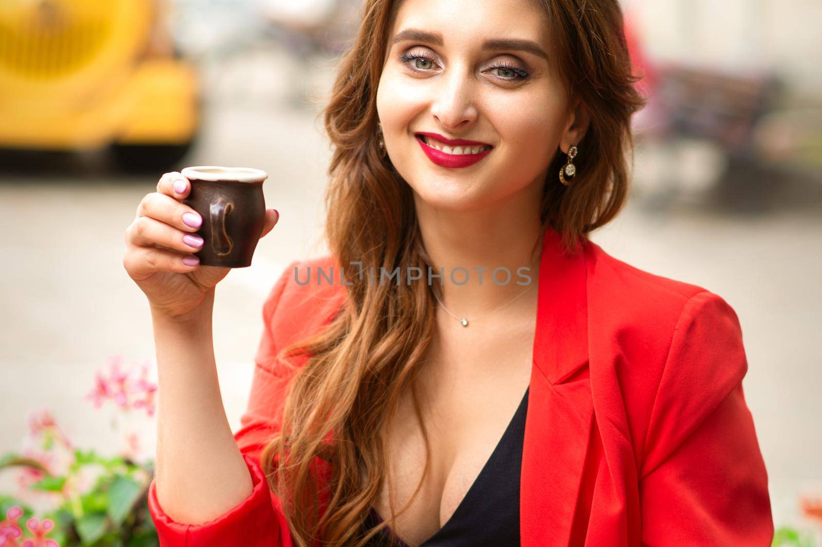 Portrait of a beautiful young smiling caucasian woman looking at the camera sitting with a cup of coffee in a cafe outdoors