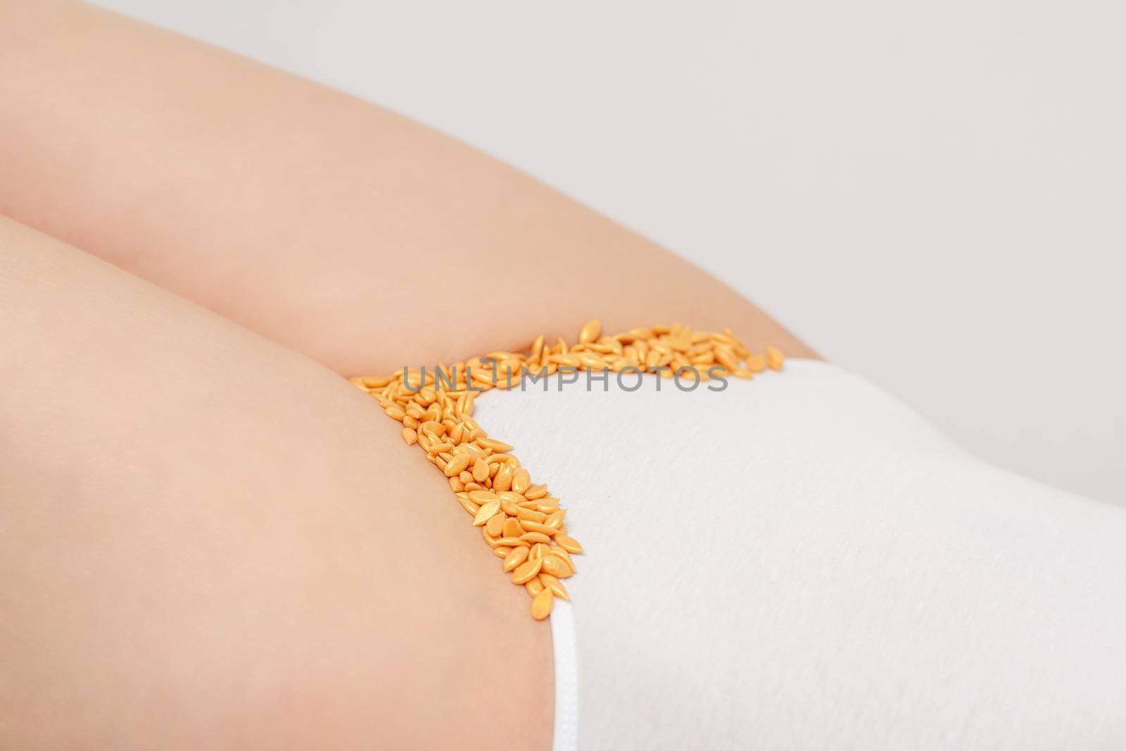 Depilation of the bikini area. Bikini zone of a young woman with wax hard beans lying down on a white background