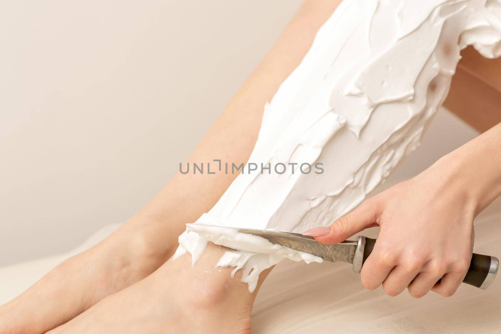 Beautiful young funny caucasian woman shaving legs with knife sitting on a white background