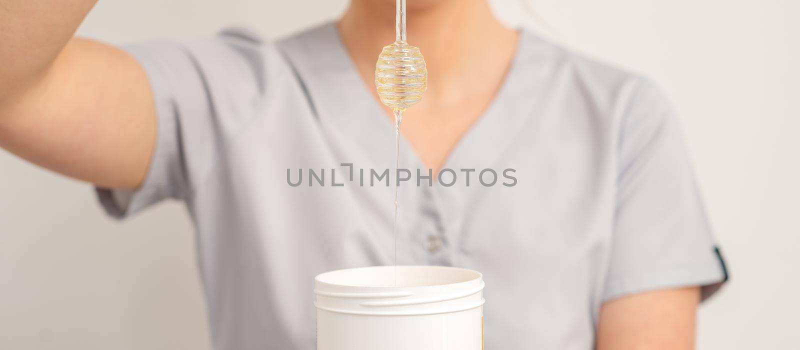 Beautician holding white bowl with wax flowing down from honey stick on a white background