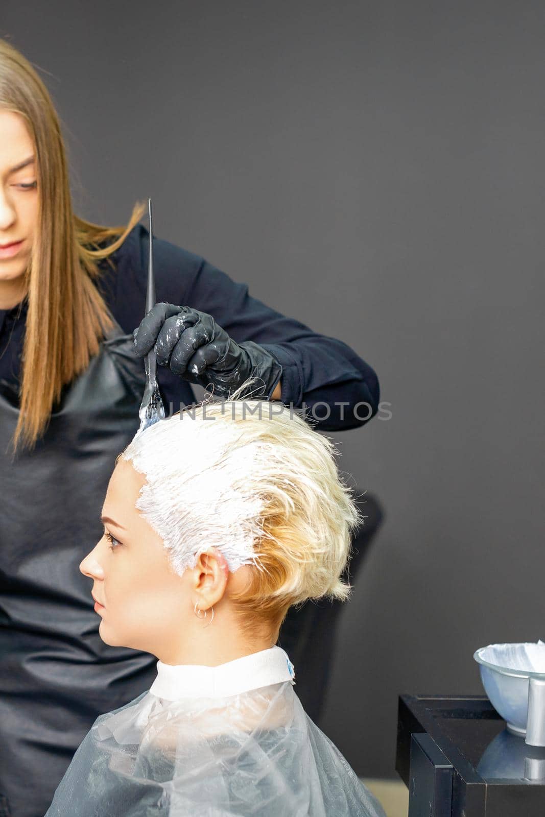 Female hairdressers dyeing hair of young caucasian woman in hair salon