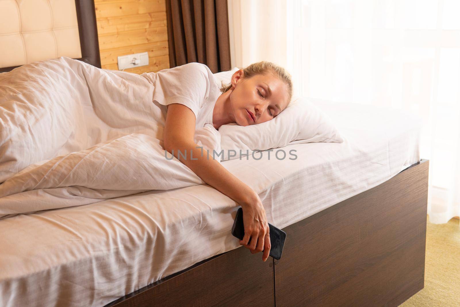 Woman blonde sleep mobile phone beautiful bed blanket view lying, from adult relax for people and smile rest, positive healthy. Indoors breathing pleasure, lie