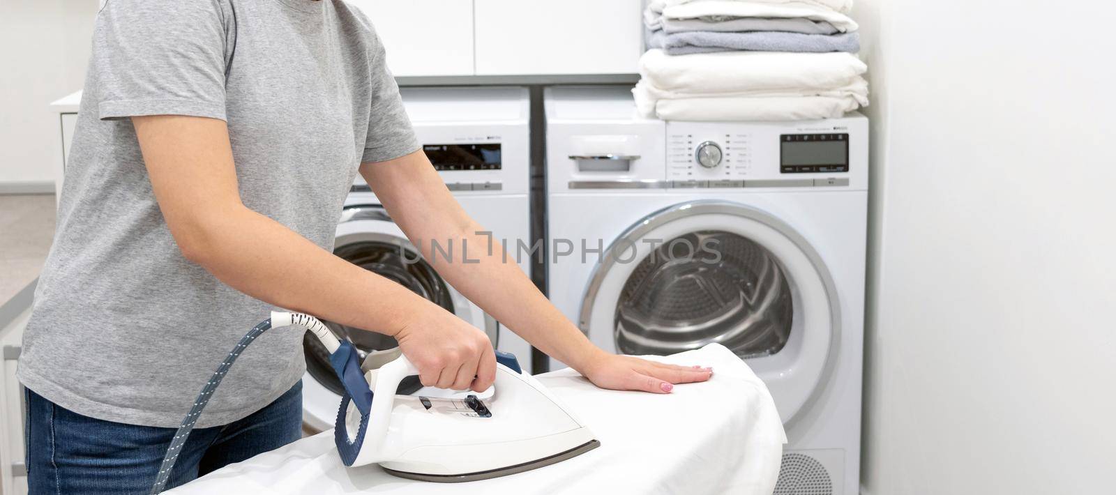 Woman ironing white shirt on board in laundry room with washing machine