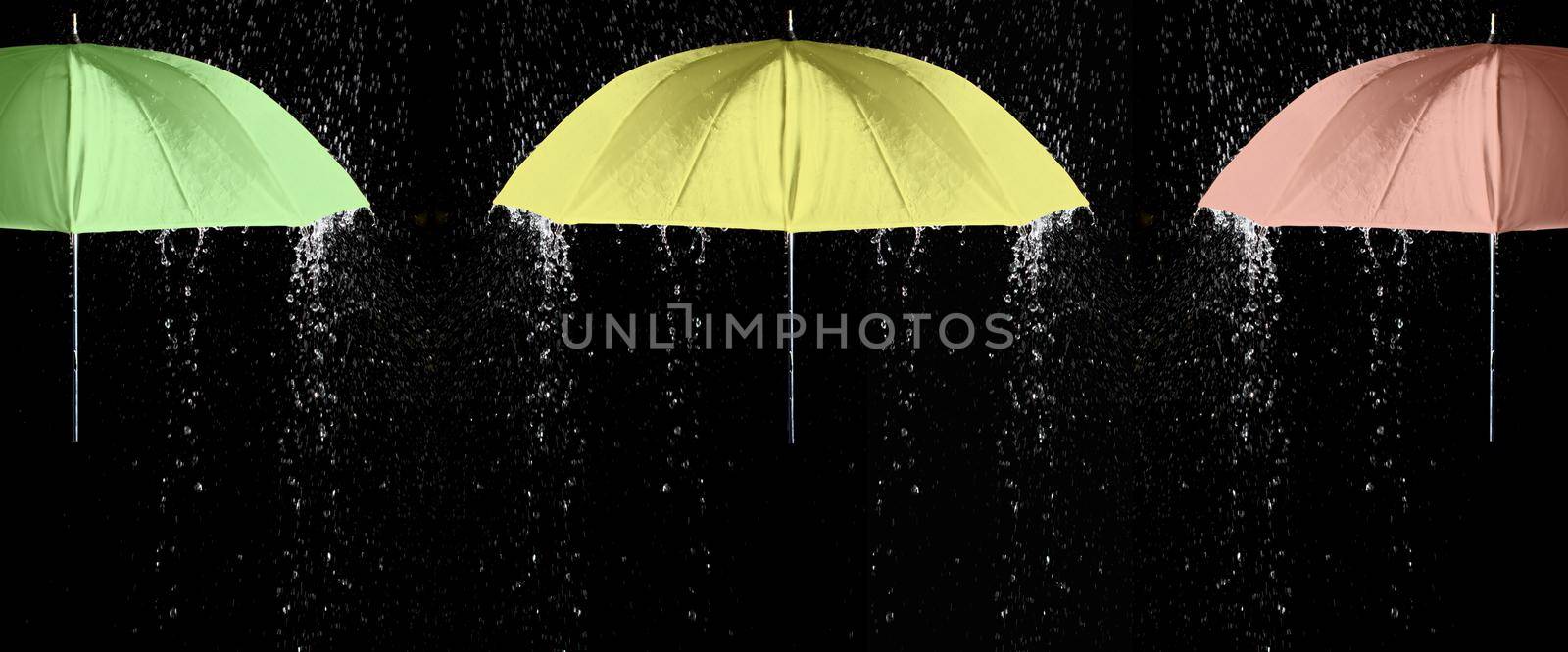 Green, yellow and red umbrellas under raindrops with black background. Business and fashion concept.