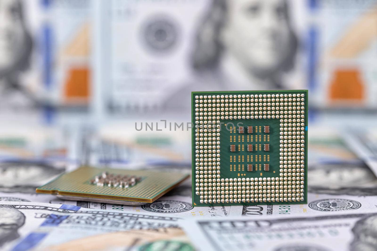 Two old computer processors lie in a pile of hundred-dollar bills