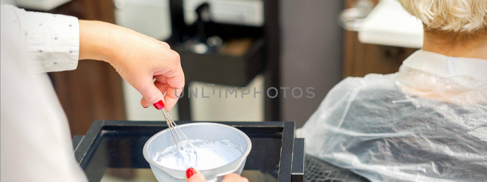 The hairstylist makes a white color dye mix for coloring hair at a salon close-up.