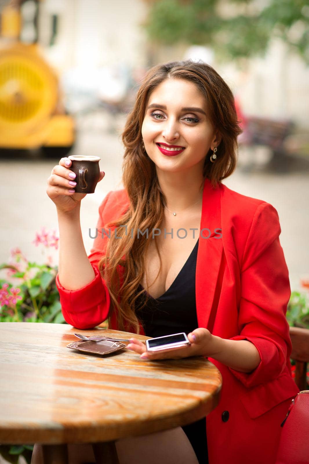 Portrait of a beautiful young smiling caucasian woman sitting at the table with a cup of coffee in a cafe outdoors