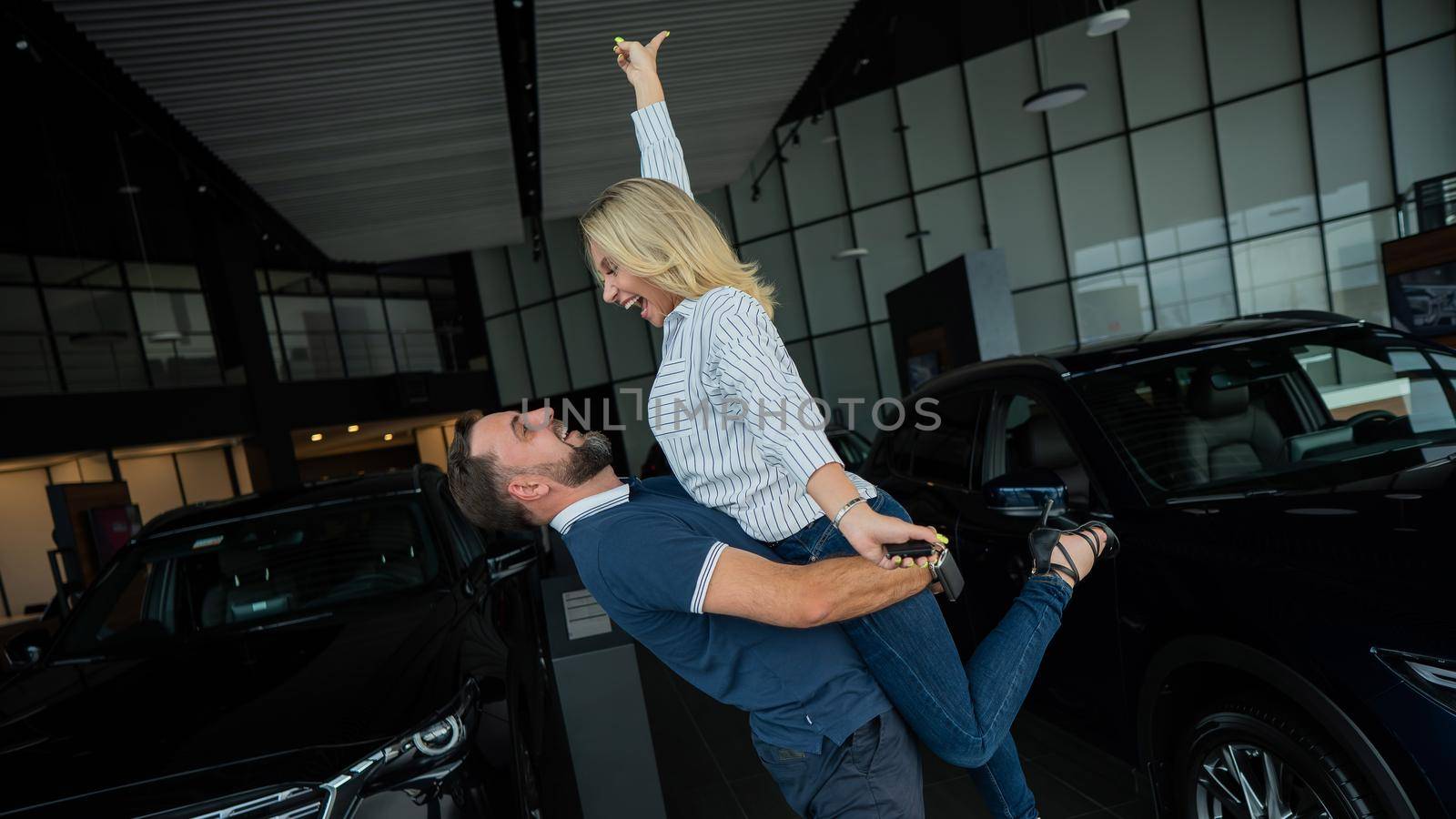 Happy caucasian couple hugging while buying a new car in a car dealership. by mrwed54