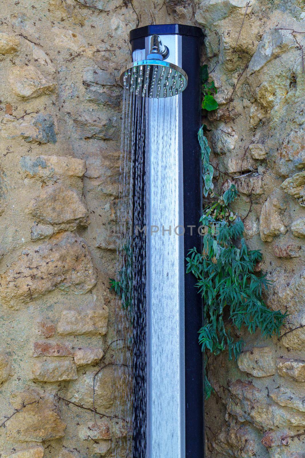 outdoor shower with a trickling stream of water and a stone wall with plants in the background