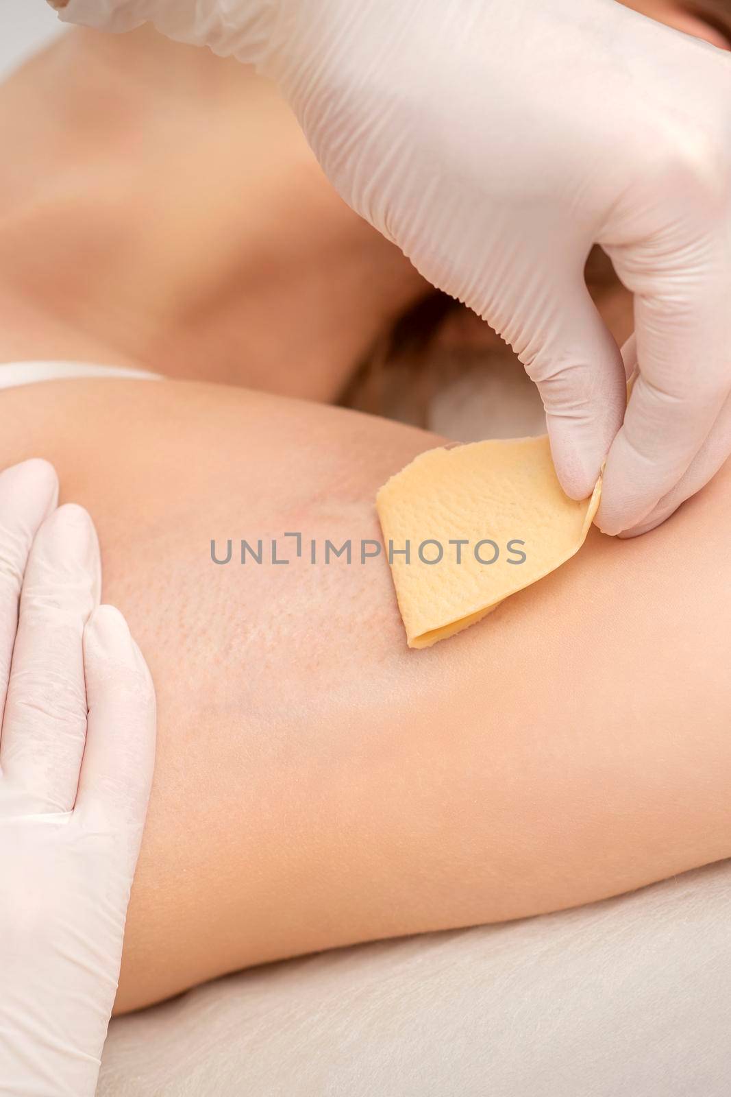 Close up of hands in gloves of beautician waxing young female armpit with sugar paste in hair removal salon