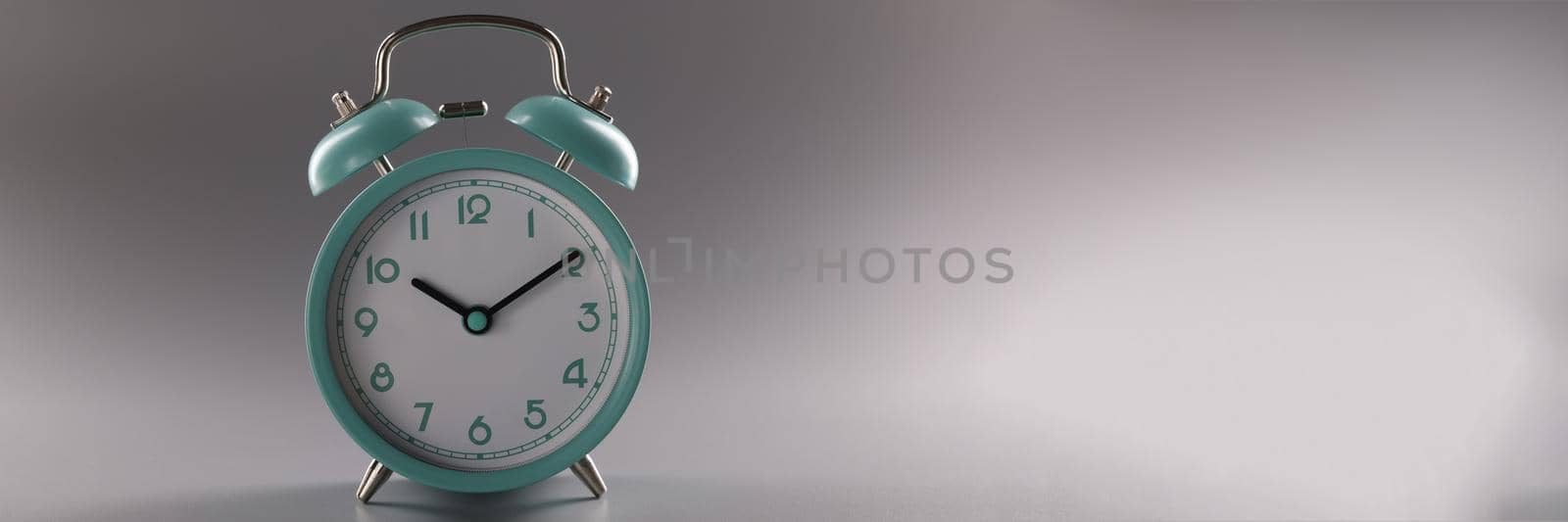 Close-up of single simple designed green retro clock on grey surface. Metal vintage clock on tiny legs stand. Time, timer, alarm, decor, rarity concept