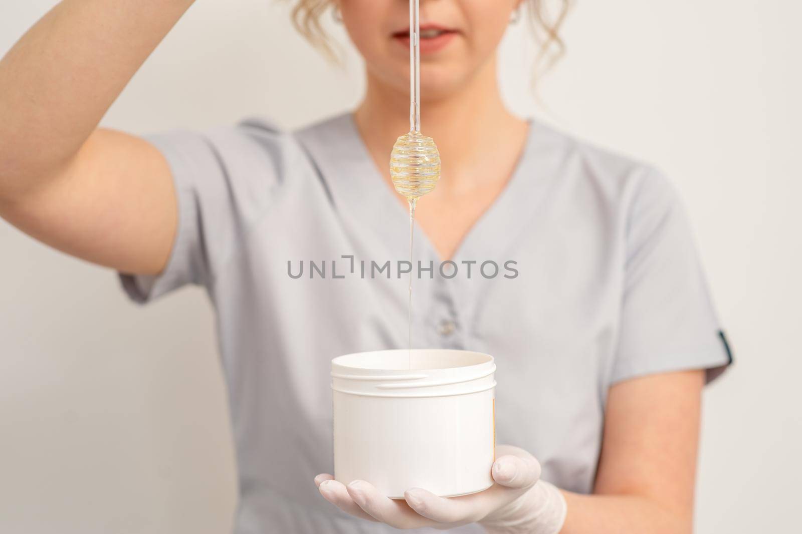 Beautician holding white bowl with wax flowing down from honey stick on a white background
