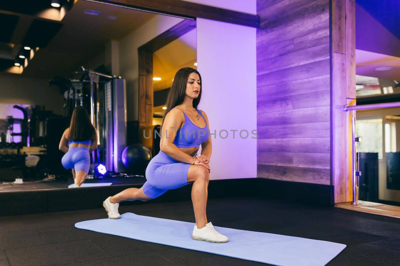 young beautiful sports woman in the gym doing exercises on a mat, in front of a mirror, arm swing, squats, fitness, yoga, in sportswear