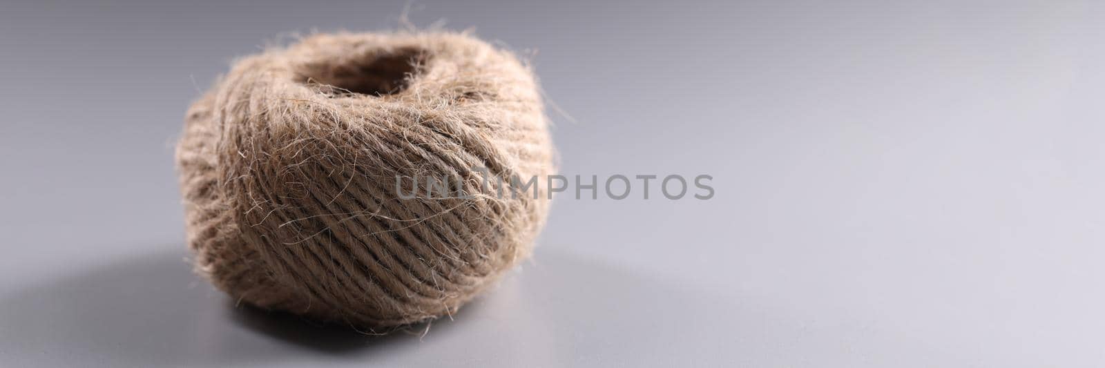 Close-up of brown rope roll, skein of jute twine on grey background. Ball of tangled thread. Hobby, equipment, knitting, needlework, handicraft concept