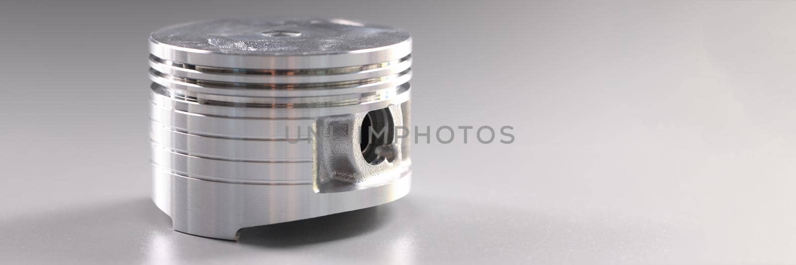 Close-up of metal new part for internal combustion engine placed in grey background. Piston detail for automobile vehicle. Transport, component concept