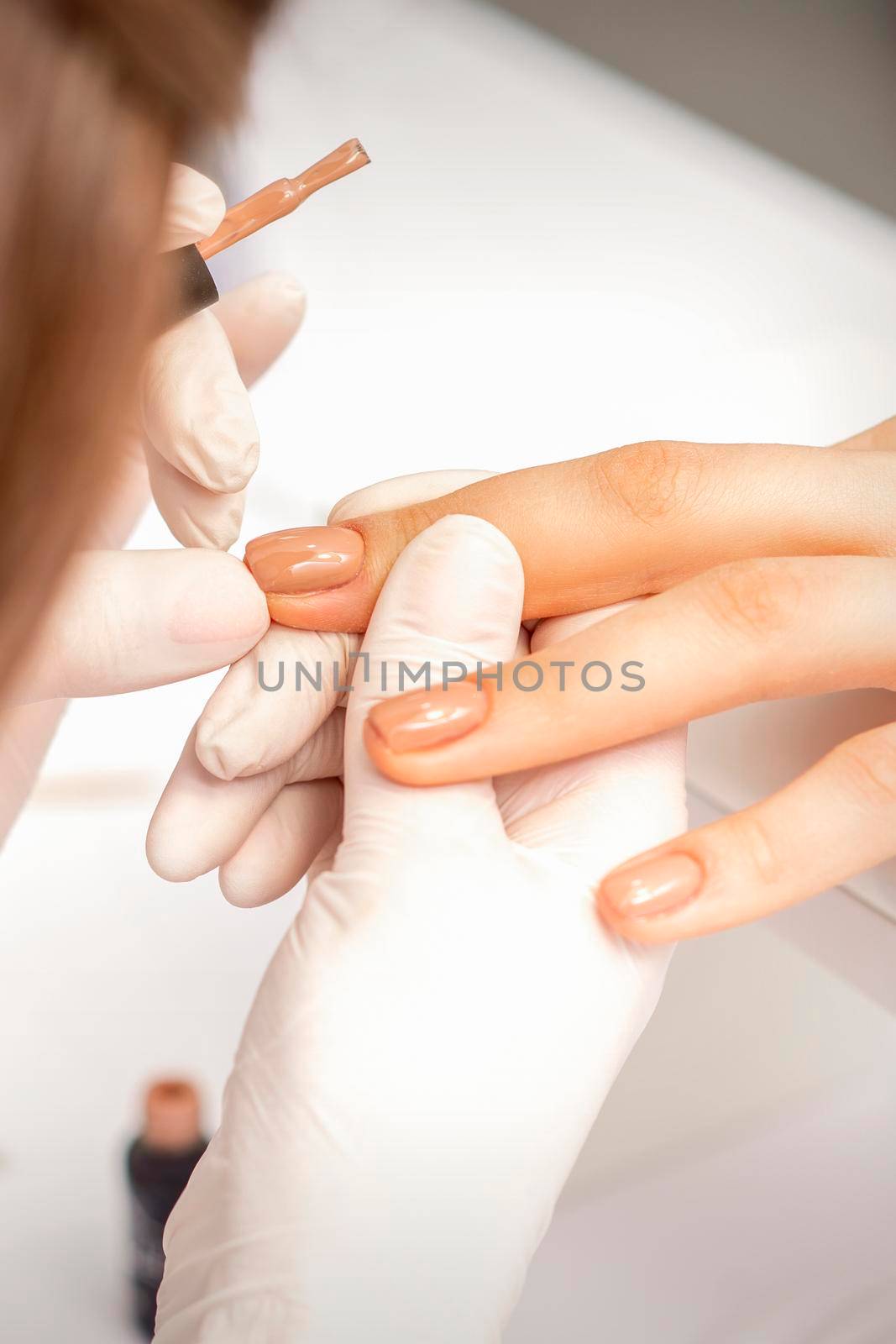 Manicurist applying beige nail polish on fingernails of a female client in a nail salon