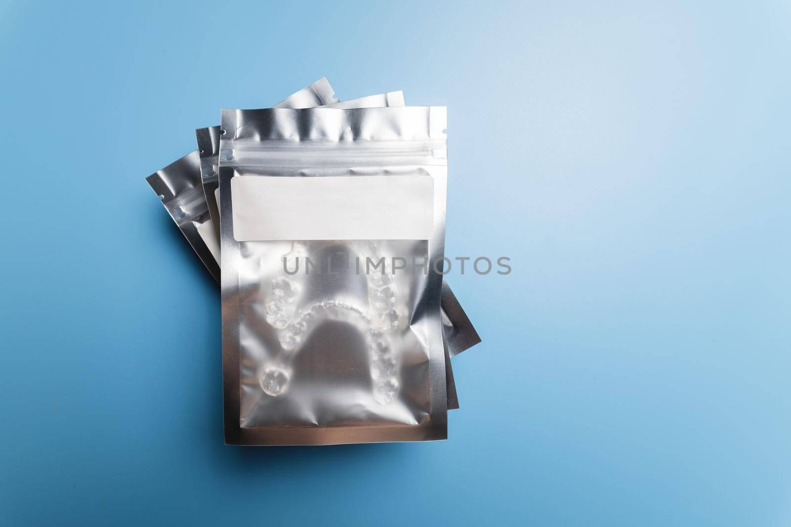 Silver plastic package body with transparent braces inside on a blue background. Invisible removable retainers for orthodontic treatment.