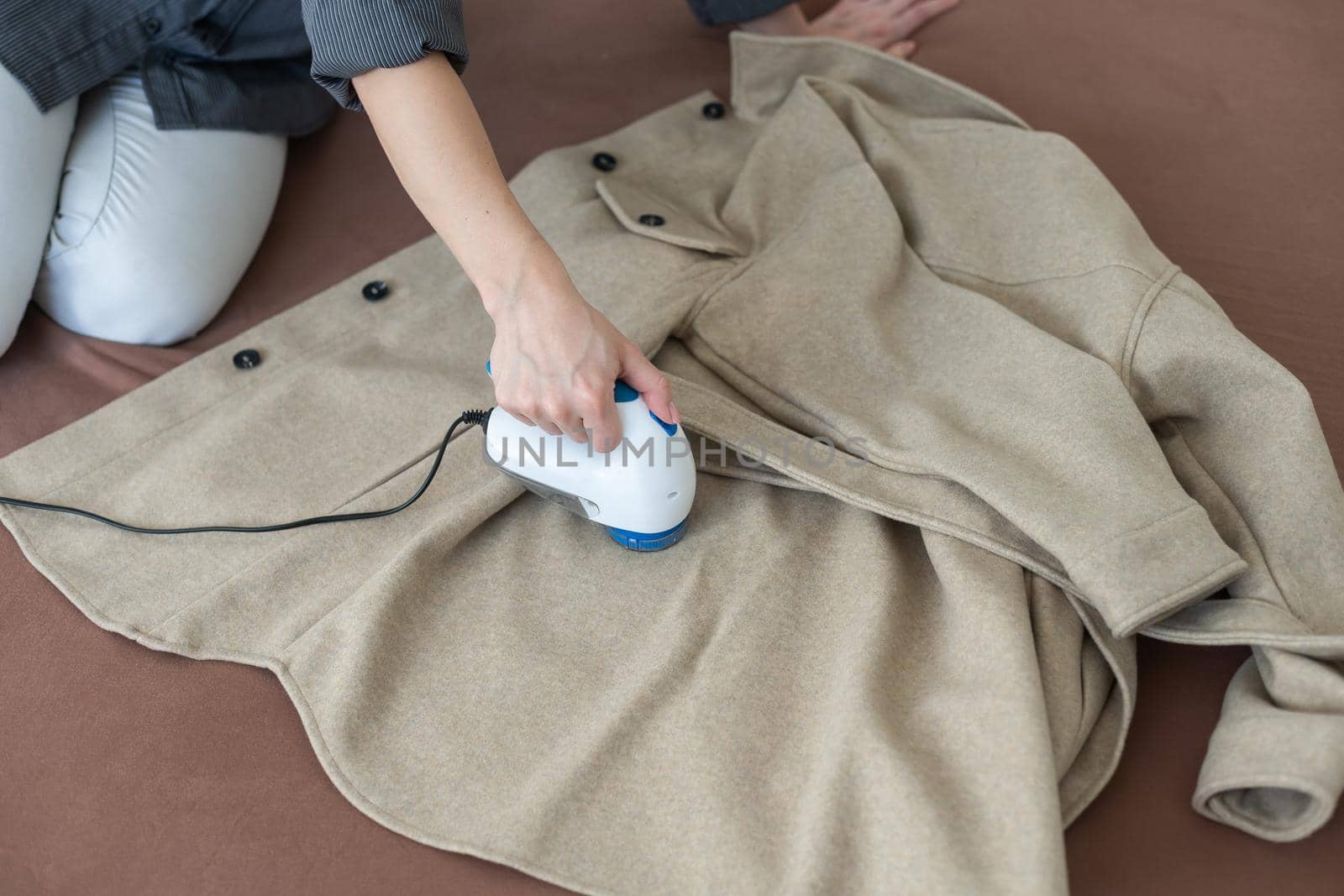 woman uses a machine for removing pellet and spools from clothes and fabric on black trousers. A modern electronic device for updating old things.