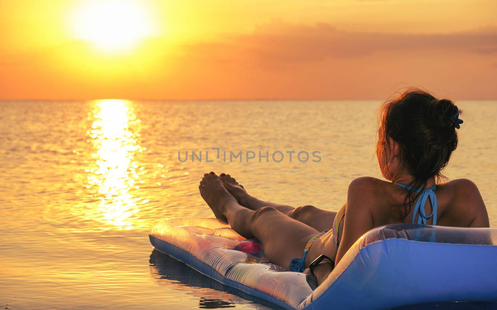 Young woman wear bikini lies on inflatable mattress on sunset orange color background. Summer vacation sea rest sun tan concept by igor010