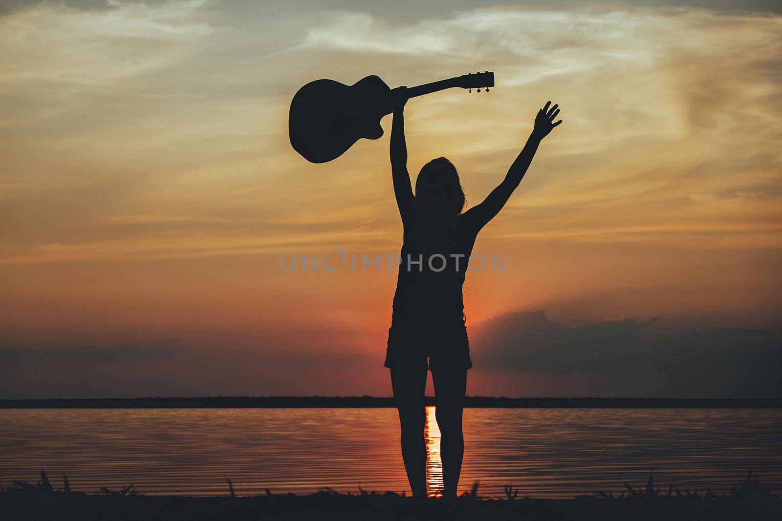 Silhouette woman with guitar in the sunset. Musician holding guitar in hand of silhouette on sunset by igor010