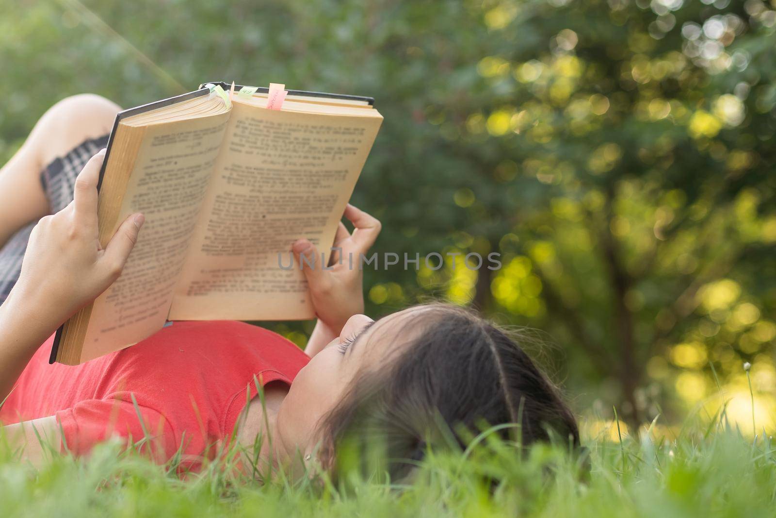 Little girl with a book in the garden. Kid is readding a book on hands. outdoors in summer day. Countryside.