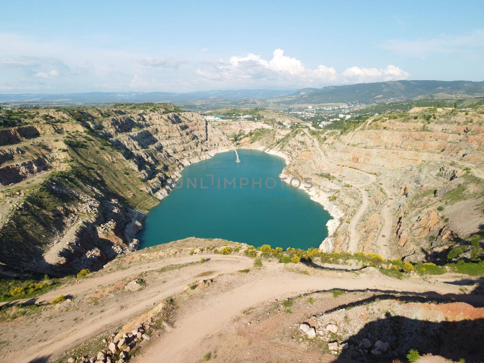 Flight over the turquoise surface of the lake in the center of the quarry. Industrial of opencast mining quarry with flooded bottom. Small lake in the shape of a heart