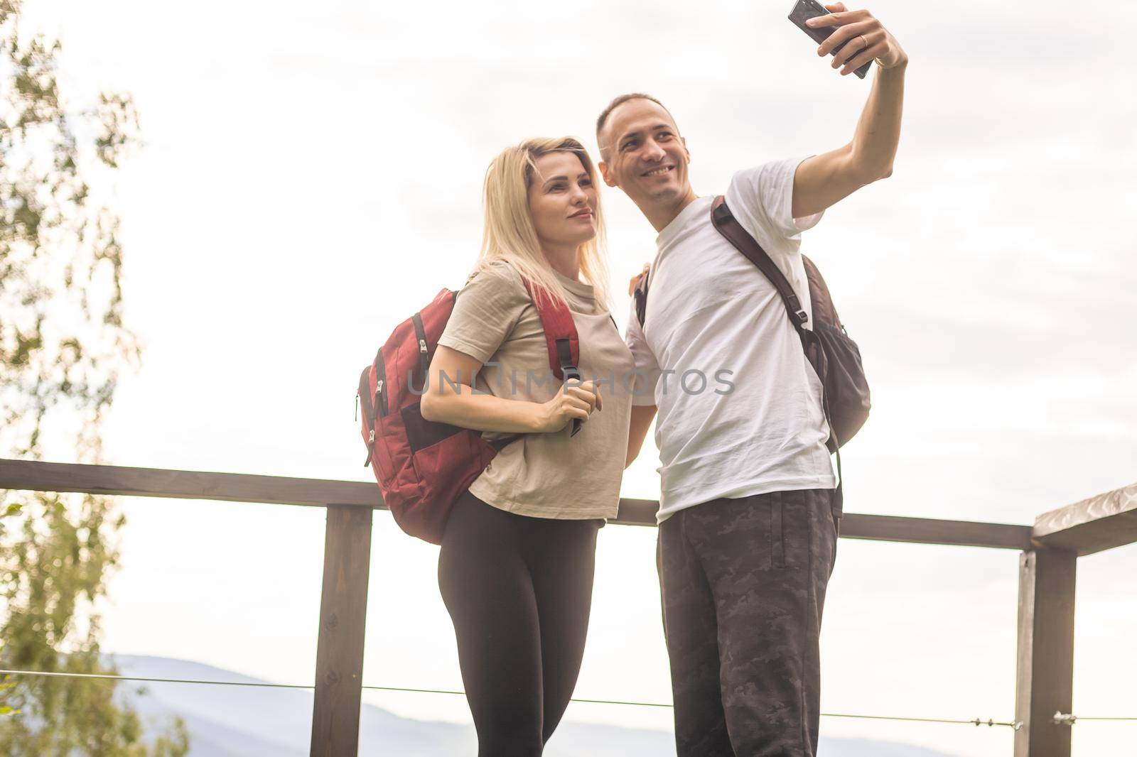 A man and a woman in tourist equipment are standing on a rock and admiring the panoramic view. A couple in love on a rock admires the beautiful views. A couple in love is traveling. A couple on a hike