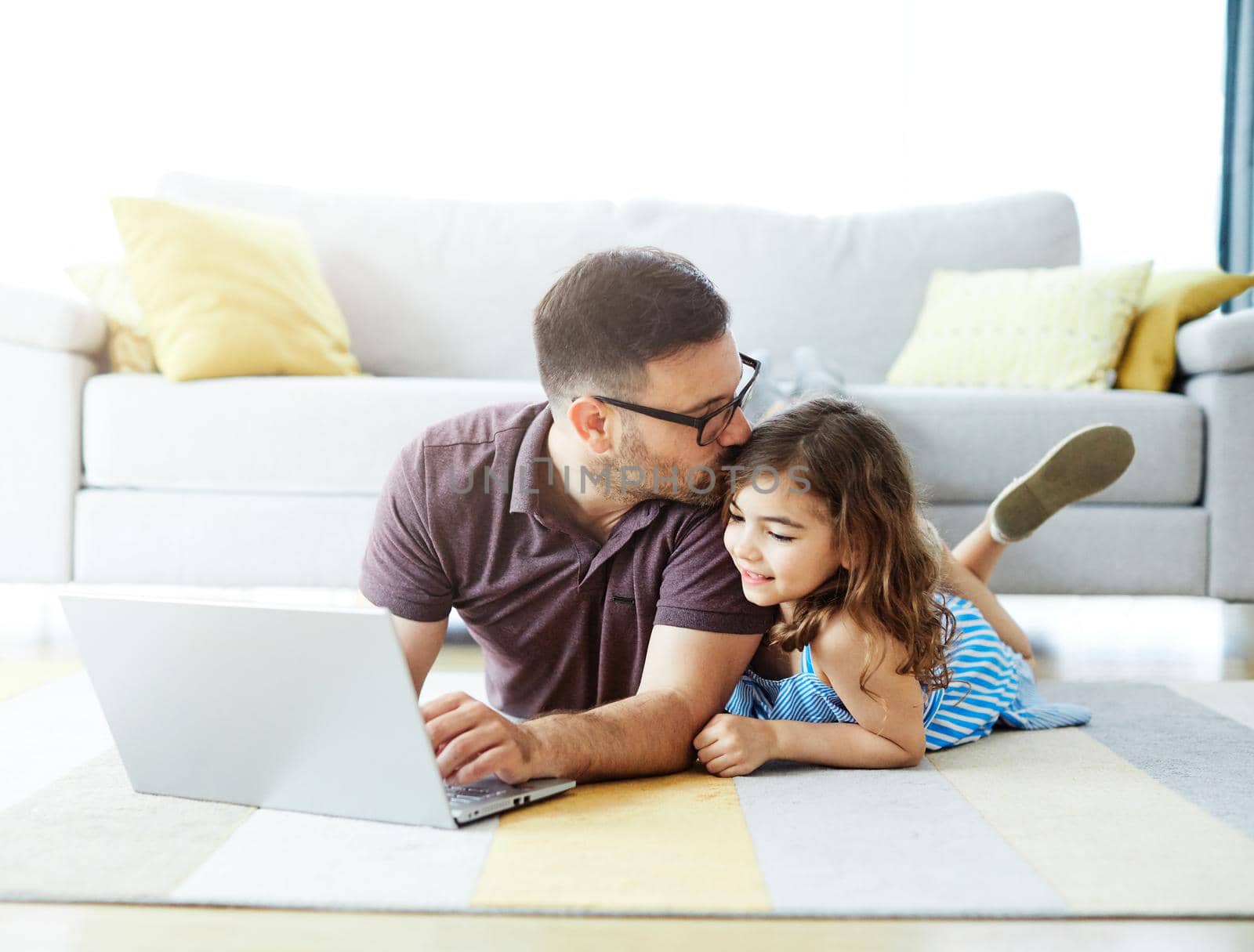 father and daughter using laptop lying down on the floor in the living room