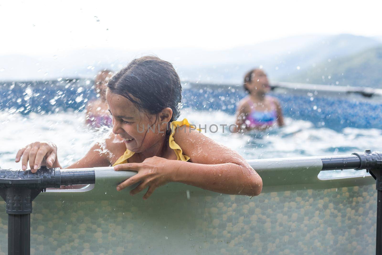 Smiling cute little caucasian girl in outdoor pool in sunny day. The girl is holding on to the side of the pool. Summer, vacation and health care concept. Space for text.