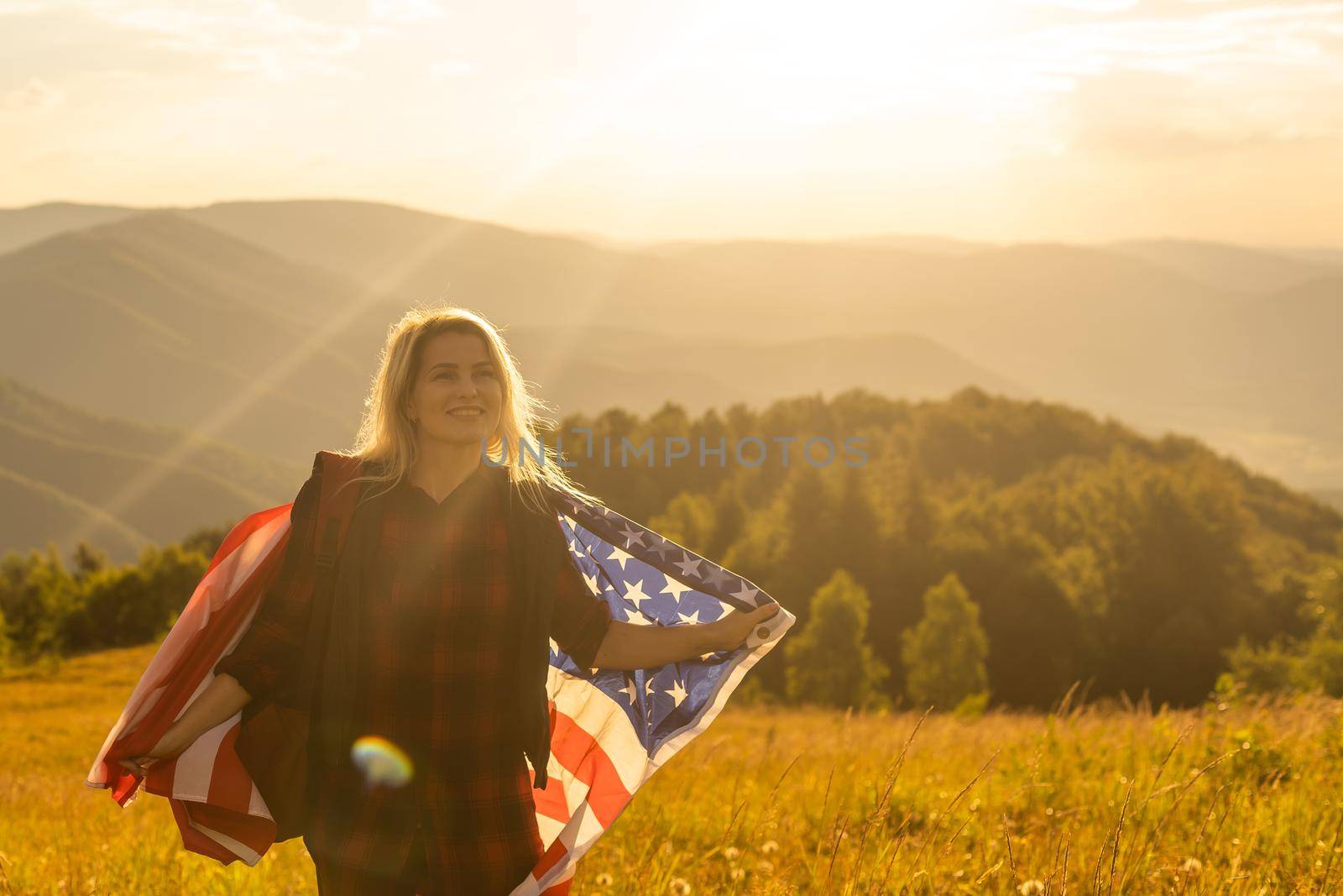 Young happy girl running and jumping carefree with open arms over wheat field. Holding USA flag.