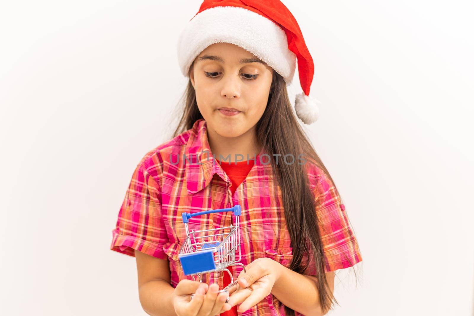 Full body little girl smiling and happy, holding a miniature shopping cart, concept of shopping, consumerism and christmas, can be used for internet purchases and commerce