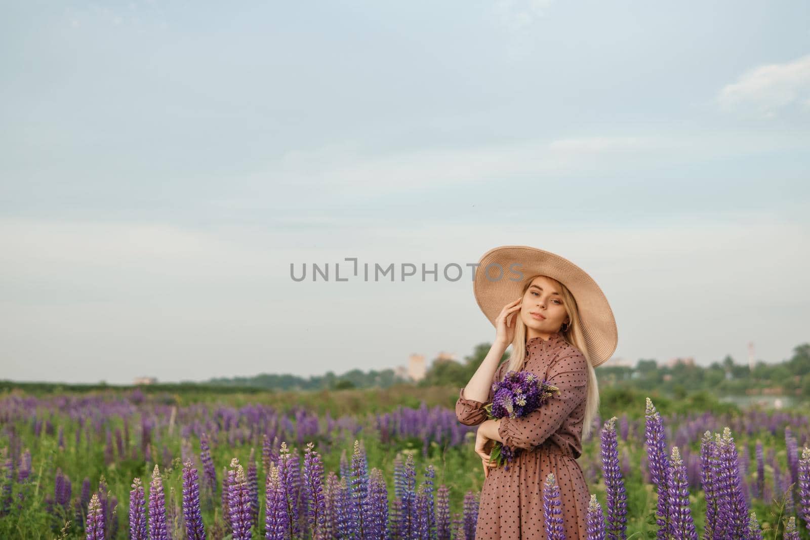 A beautiful woman in a straw hat walks in a field with purple flowers. A walk in nature in the lupin field.