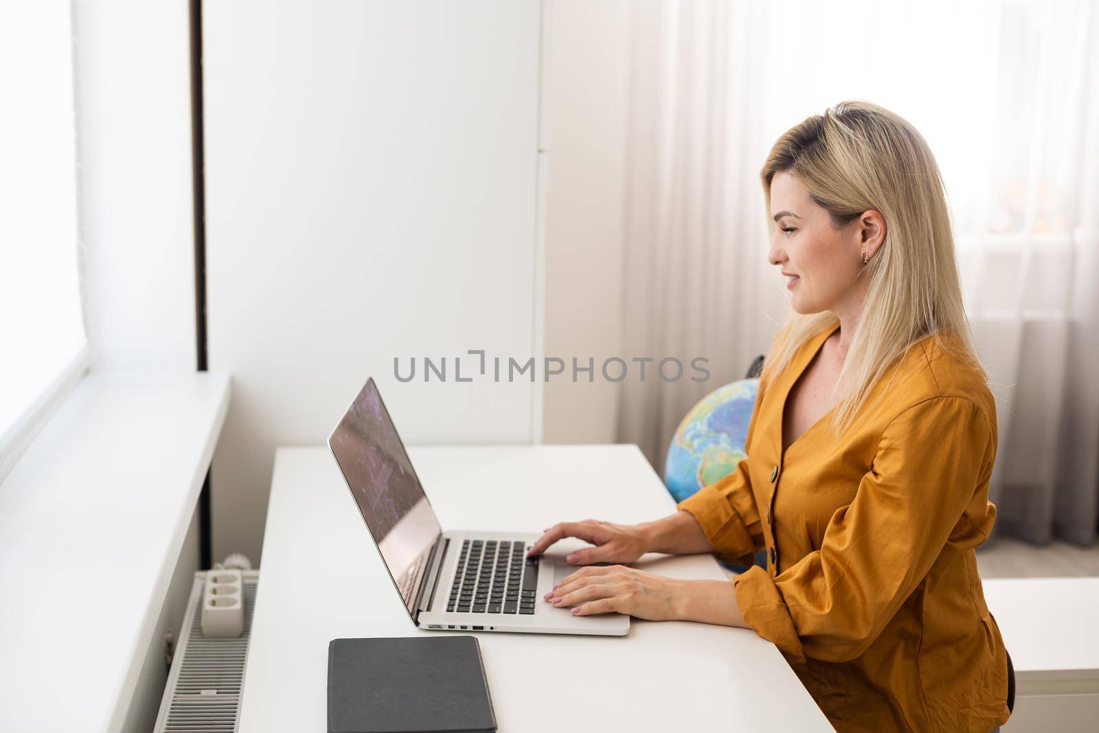 Mockup image of a woman using and typing on laptop with blank white desktop screen on wooden table