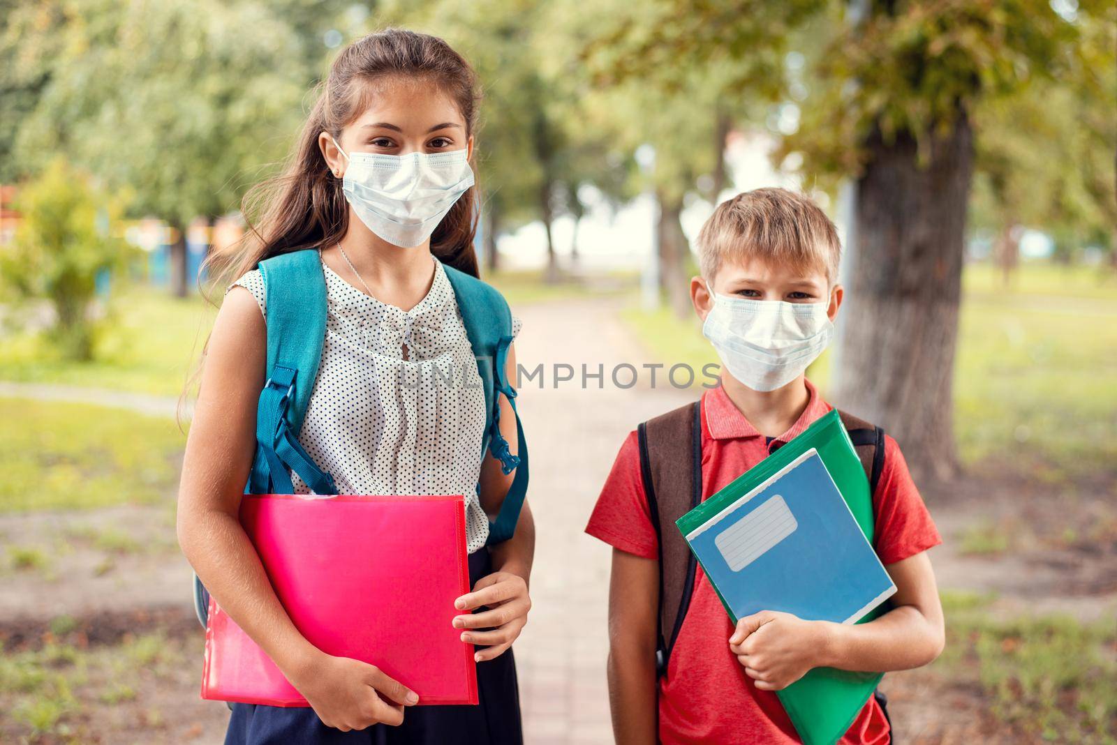 Male and female school learners going to school in the park, wearing medical masks to protect themselves from the dangerous virus