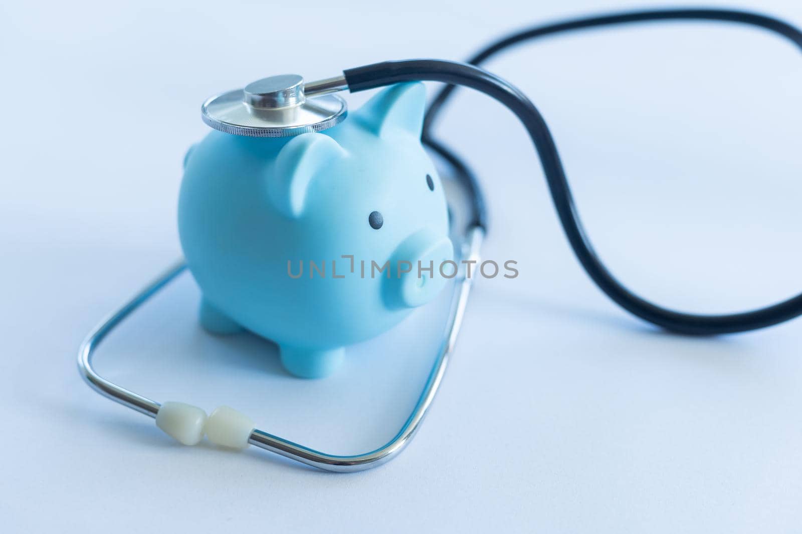 Piggy bank with stethoscope isolated on light blue background with copy space. Health care financial checkup or saving for medical insurance costs concept.