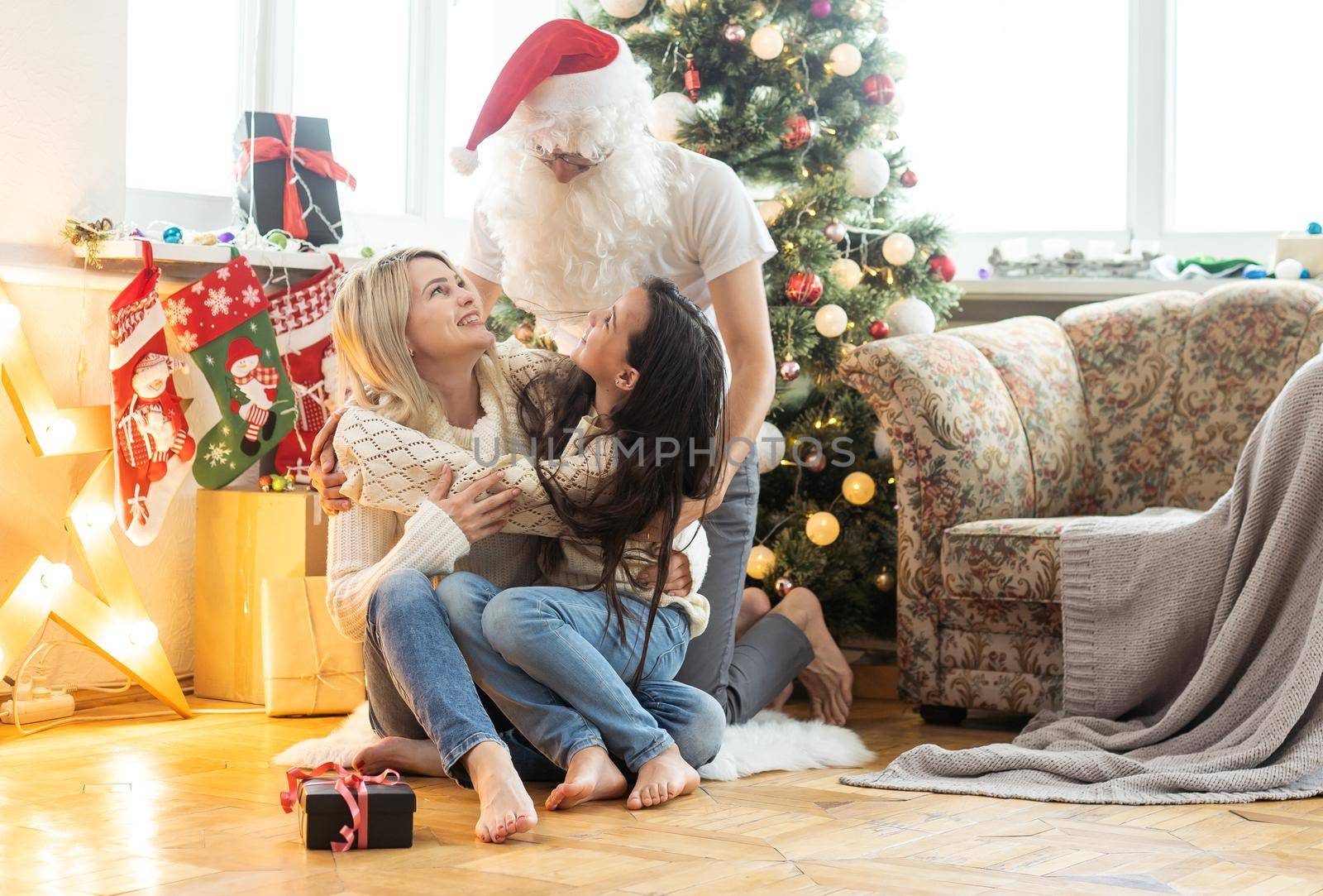 Picture of happy family celebrating New Year eve, little girl with parents enjoying winter holidays, father wearing Santa Claus costume, Christmas magic, happiness and love concept.