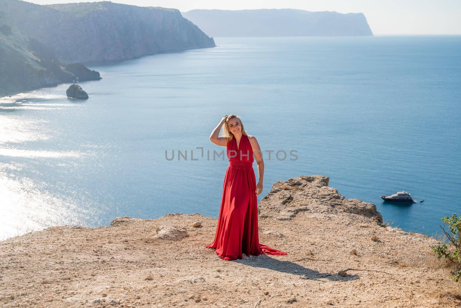 A woman in a red flying dress fluttering in the wind, against the backdrop of the sea