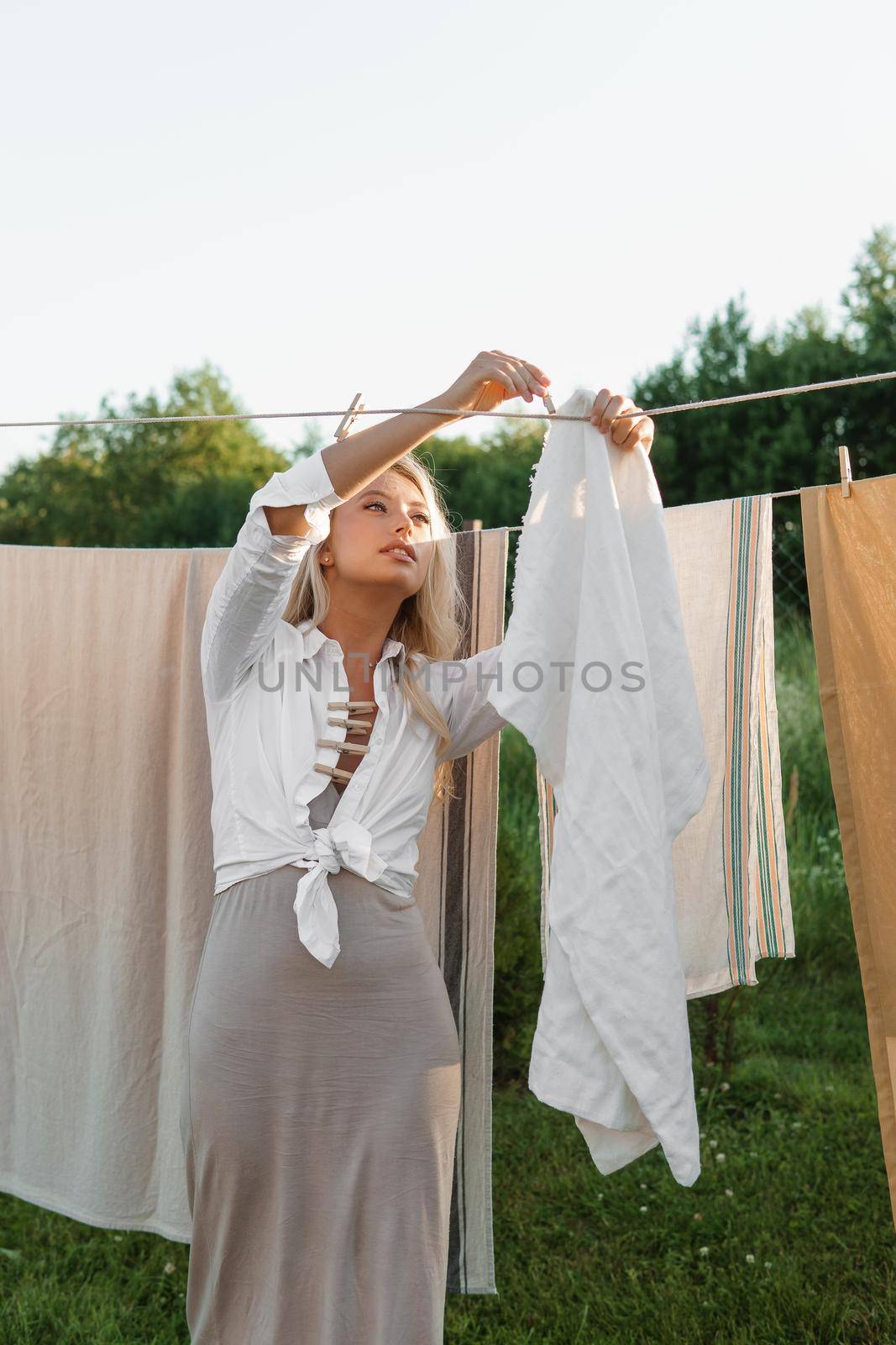Laundry day. A woman hangs linen and towels on a tree in the courtyard of a village house. Summer cottage concept.