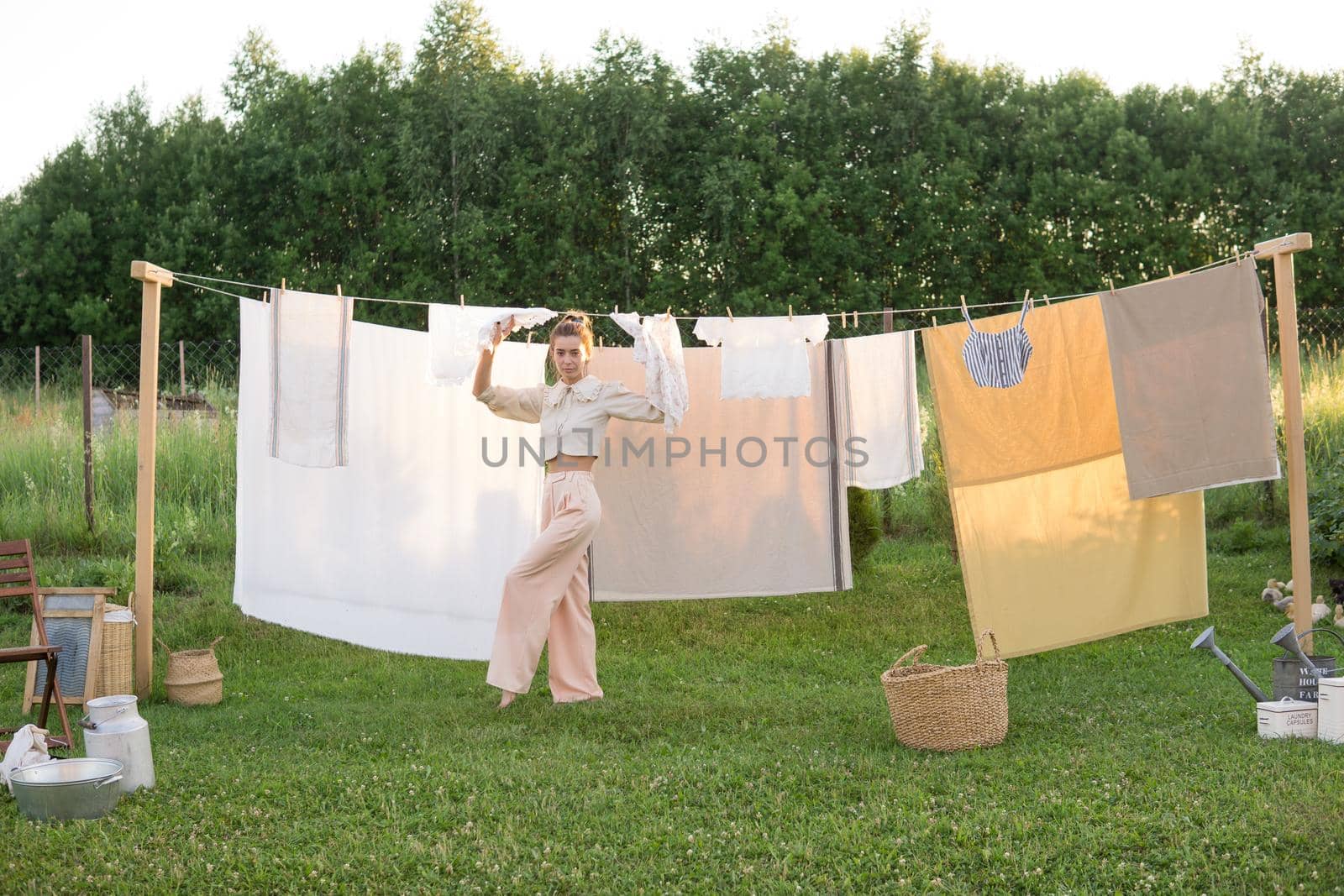 Laundry day. A woman hangs linen and towels on a tree in the courtyard of a village house. Summer cottage concept.