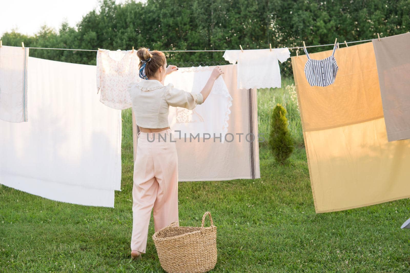 Laundry day. A woman hangs linen and towels on a tree in the courtyard of a village house. Summer cottage concept.