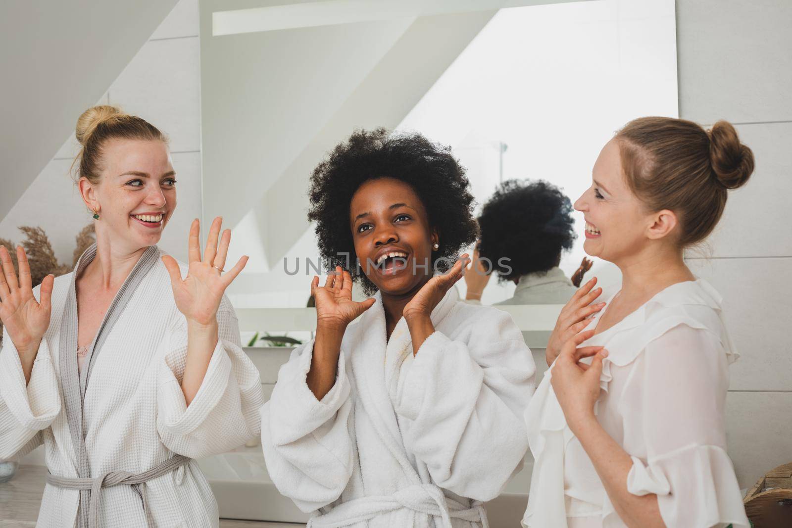 Three young girlfriends are delighted with the spa. They stand in white robes and smile
