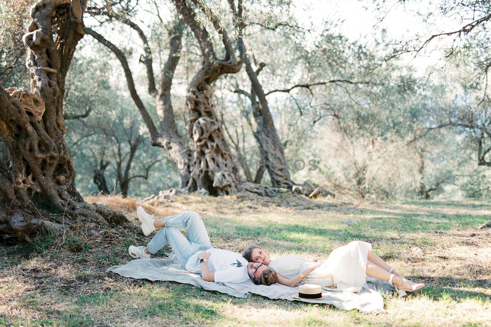 Man and woman lie head to head on a blanket in an olive grove. High quality photo