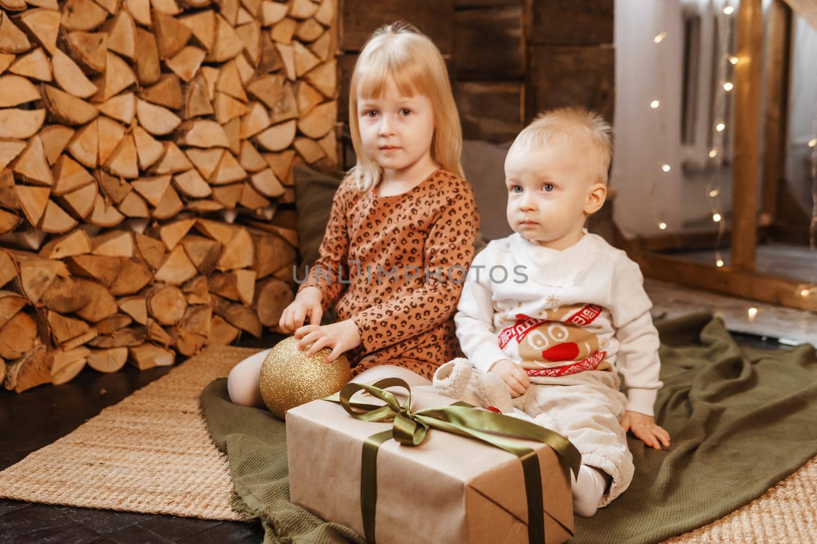 Little brother and sister play on Christmas eve in a beautiful house decorated for the New Year holidays. Children are playing with a Christmas gift. Scandinavian-style interior with live fir trees and a wooden staircase.