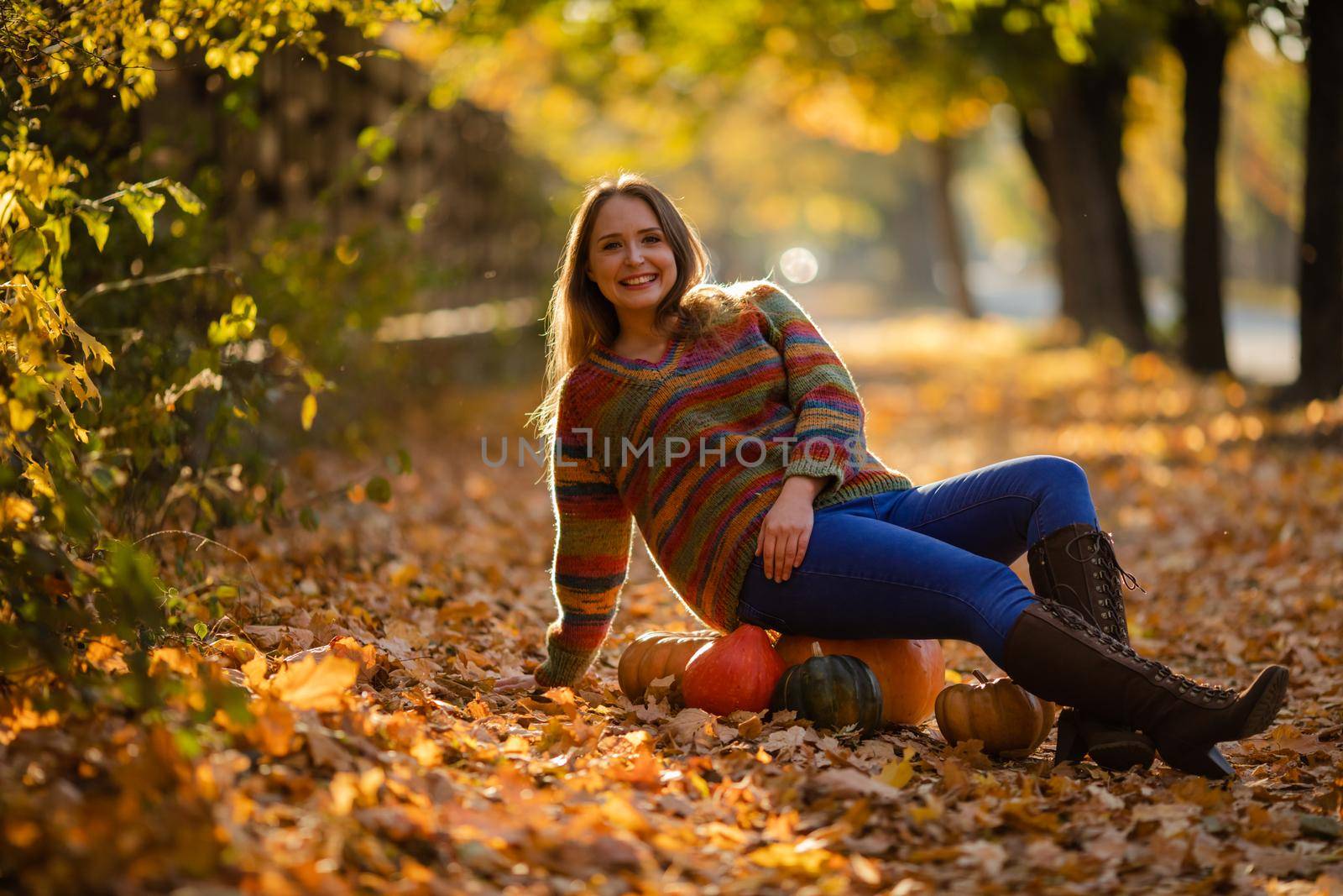 Smile woman sitting on the pumpkin on the autumanl maple leaves. Cozy autumn vibes Halloween, Thanksgiving day.