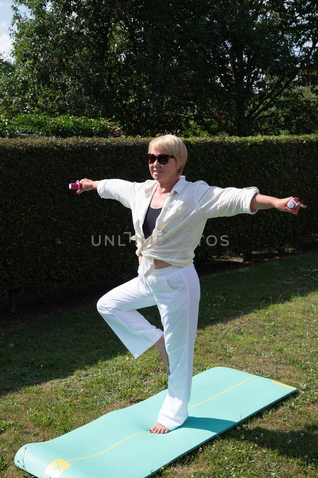 middle aged caucasian doing yoga in the garden in summer sporty lifestyle by KaterinaDalemans