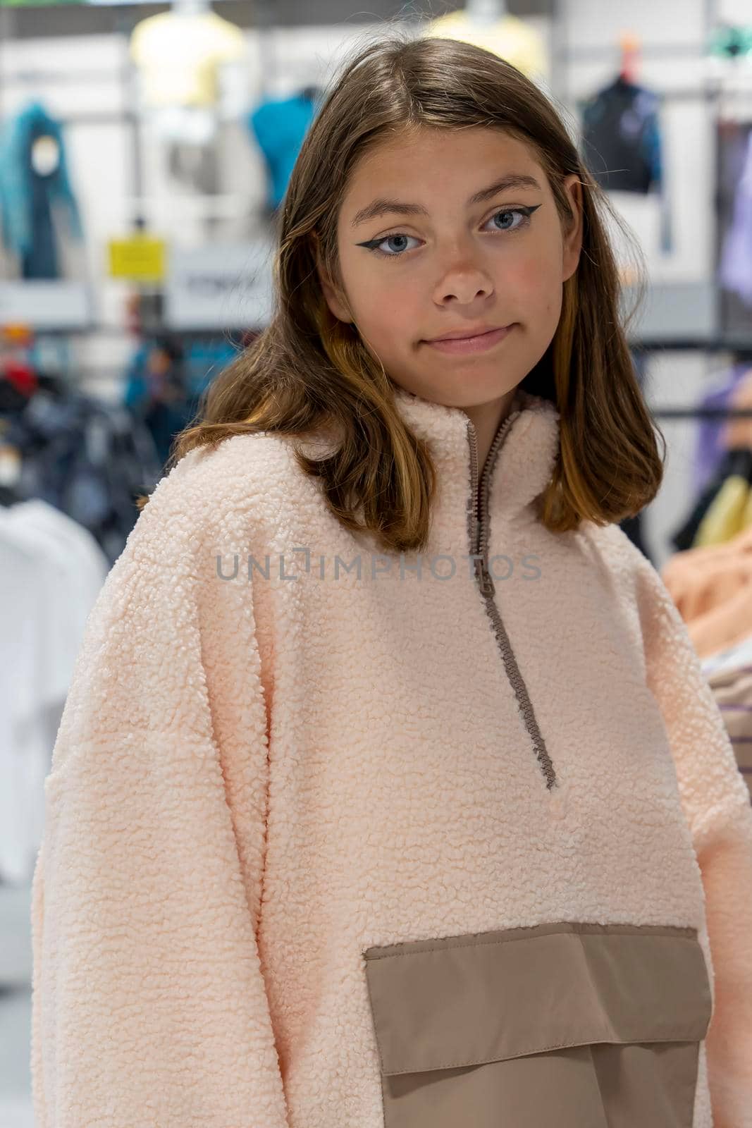 a happy beautiful girl in a clothing store tries on a fashionable sweatshirt and looks at the camera with a smile . shopping, fashion, style