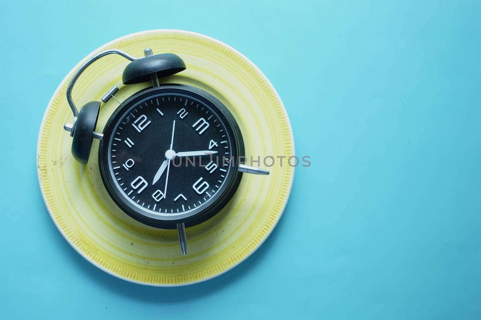 Alarm clock on plate on wooden table, top view
