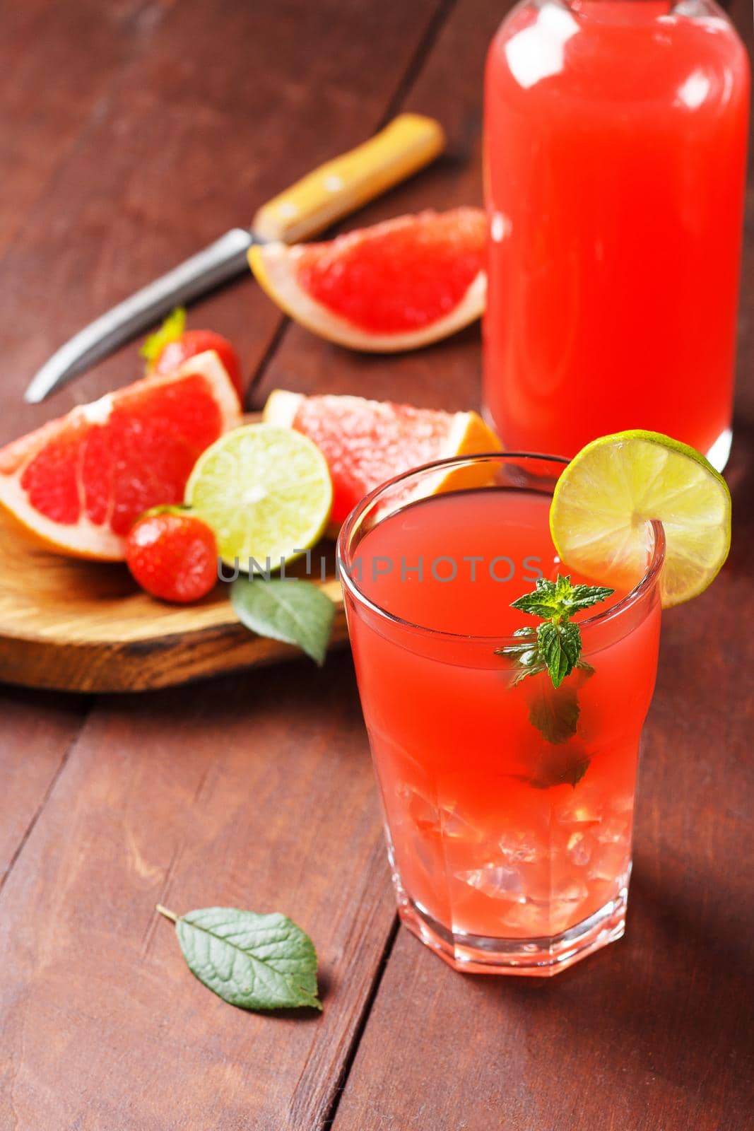 Fresh grapefruit juice in a glass with grapefruit pieces, lime and mint on a wooden background. vertical photo